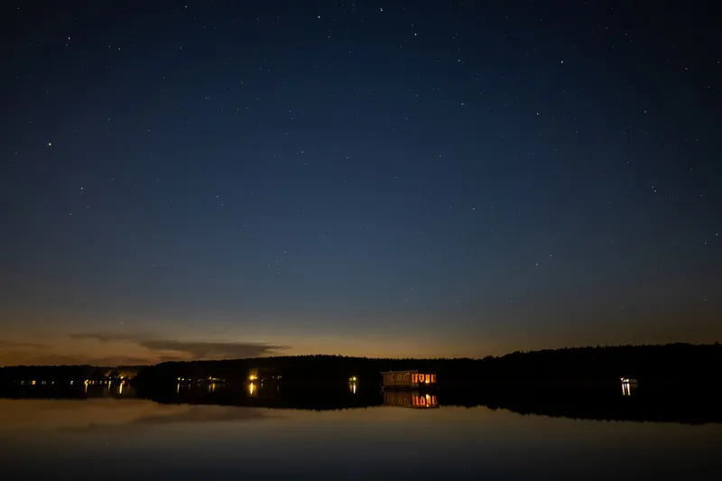 A wide starry night sky reflected in still, dark water