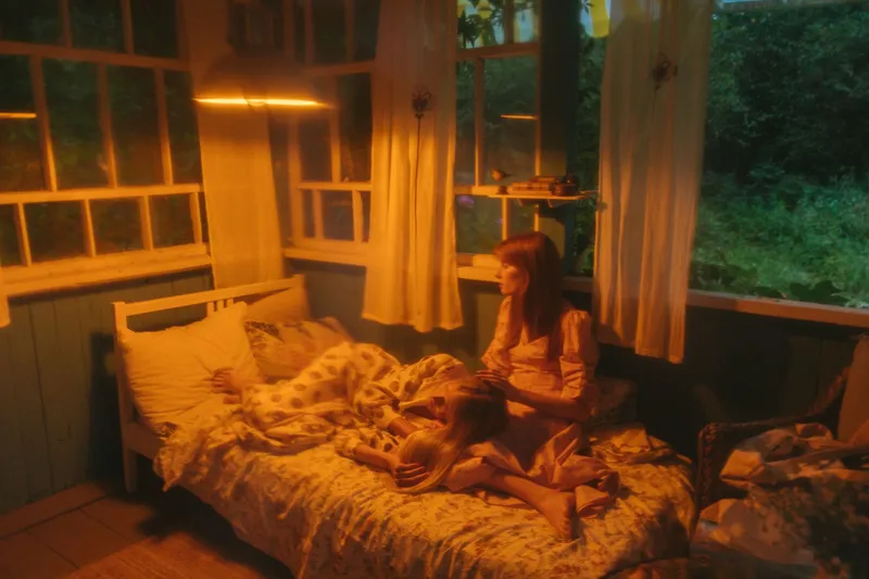 A parent sitting on the edge of a child's bed in a warmly lamplit room at night